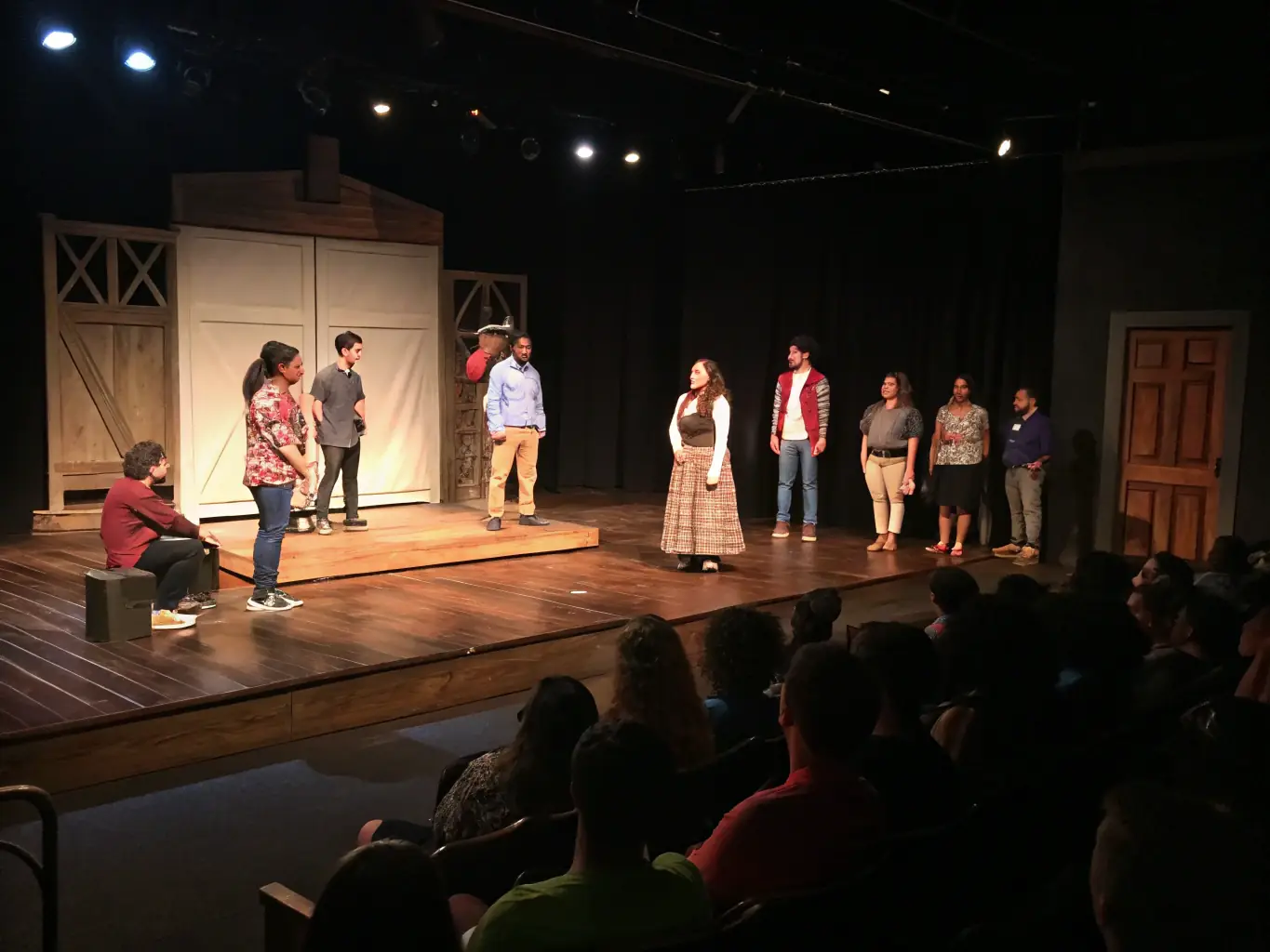 A stage performance in a local theater, with musicians and singers performing under warm stage lights, an engaged audience watching attentively, highlighting the impact of live performances on community cohesion.